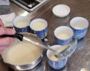 Pouring Mirin vegan pudding into pretty blue dishes