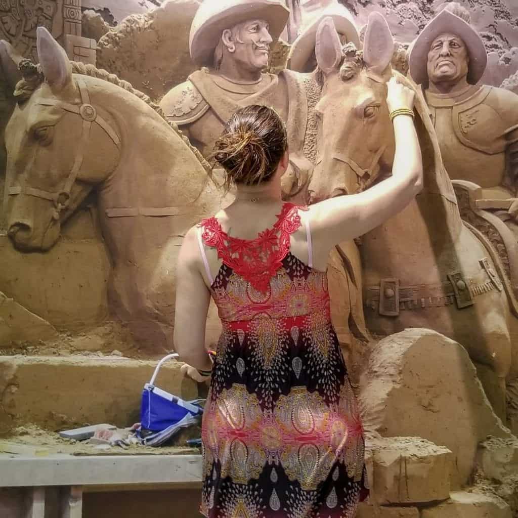 A young woman in a sundress pretends to sculpt an intricate sand statue of horses and soldiers at the Tottori Sand Museum in Tottori Japan